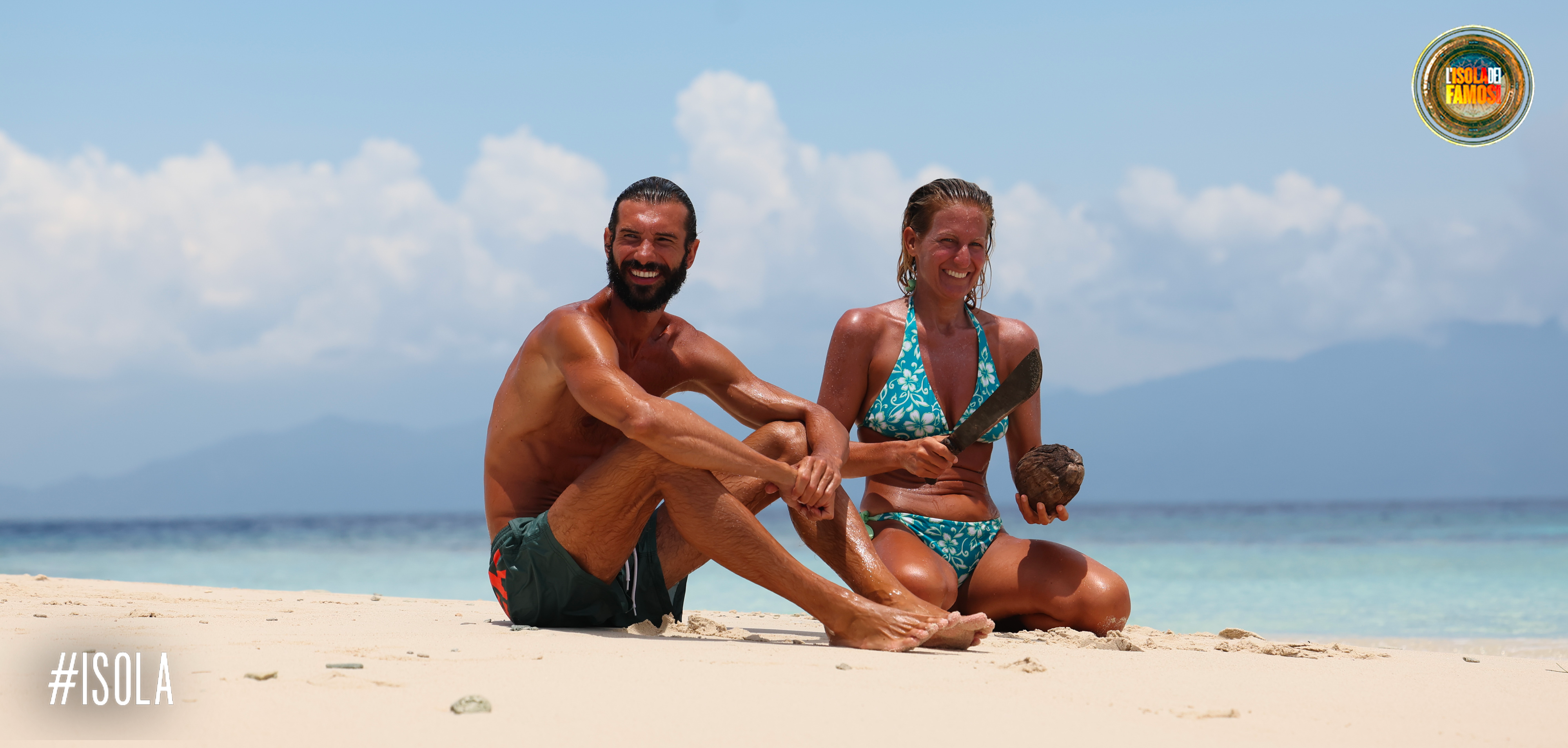 Artur e Alvina aprono un cocco in riva al mare.