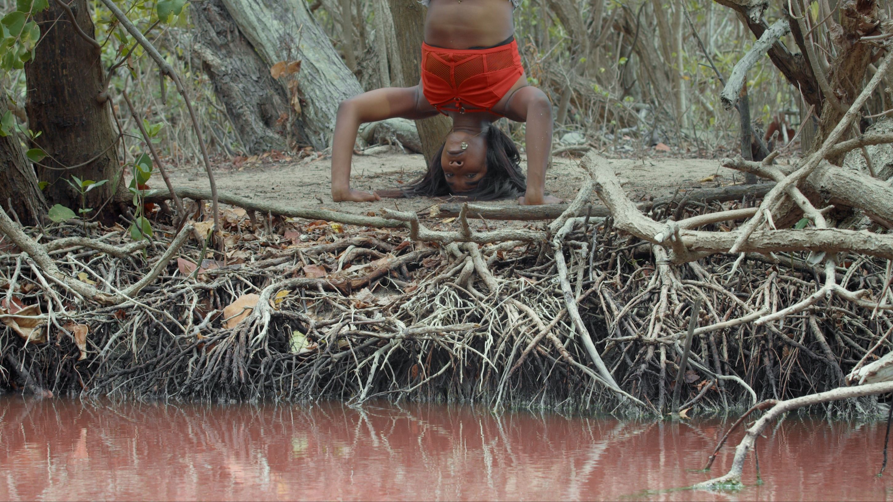 Un frame da Mangrovia (2024) di Low Jack & Invernomuto, coppia di artisti e musicisti che intrecciano suono, corpo e natura in una visione ipnotica. Il video, presentato nella mostra The Screen is a Muscle alle Gallerie d’Italia – Torino, è un viaggio sensoriale tra radici, acqua e ritmo, dove il paesaggio diventa partitura. Crediti: Courtesy of the Artist and Pinksummer, Genova

