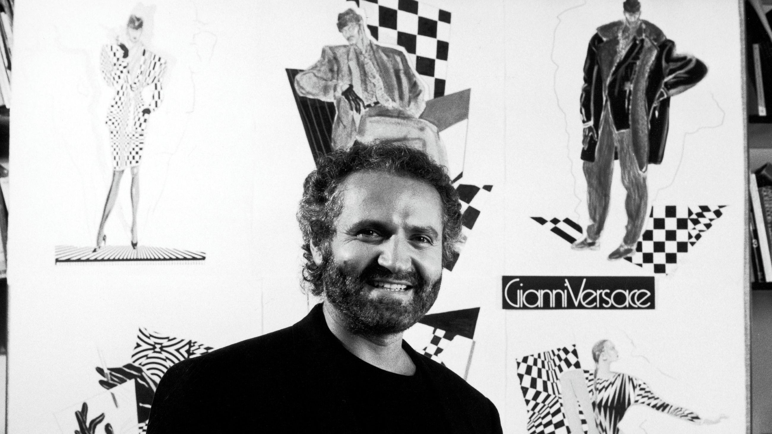 Lo stilista Gianni Versace sorride con alle spalle alcuni dei suoi bozzetti; 1986 – Credits: Getty Images