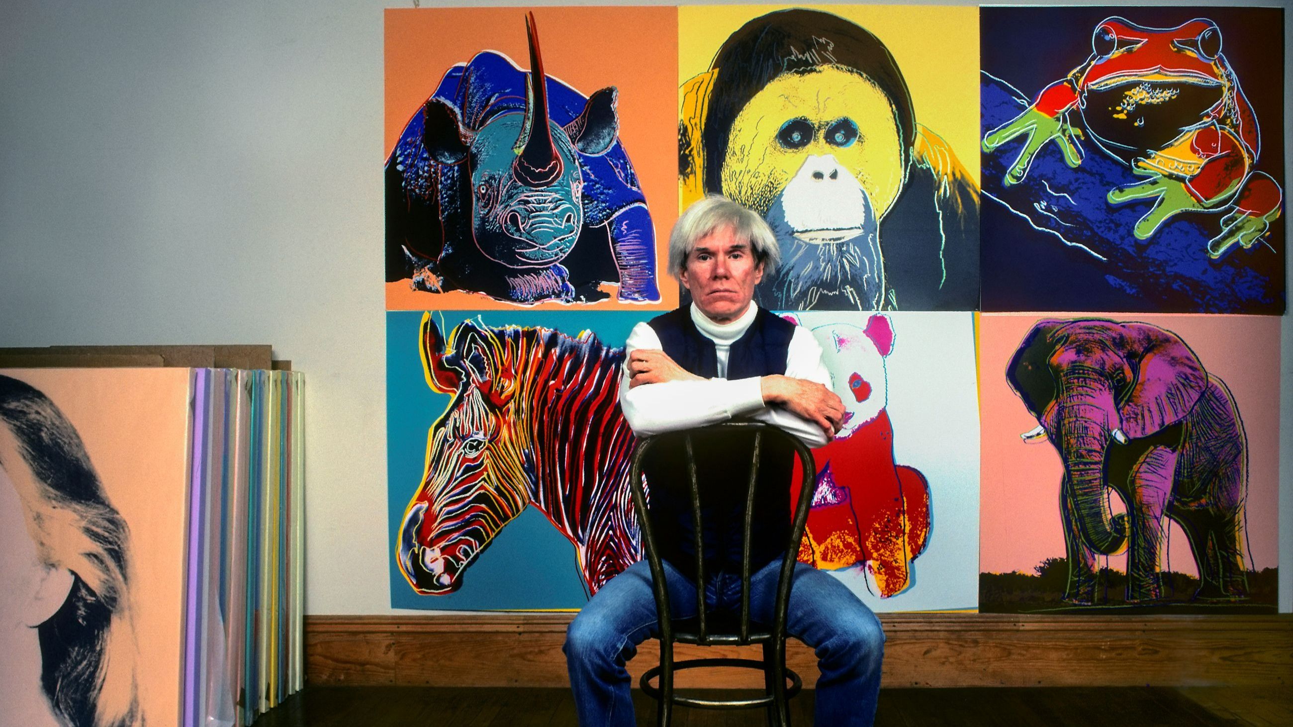Andy Warhol seduto davanti a diversi dipinti della sua serie “Endangered Species” nel suo studio - Credits Getty Images