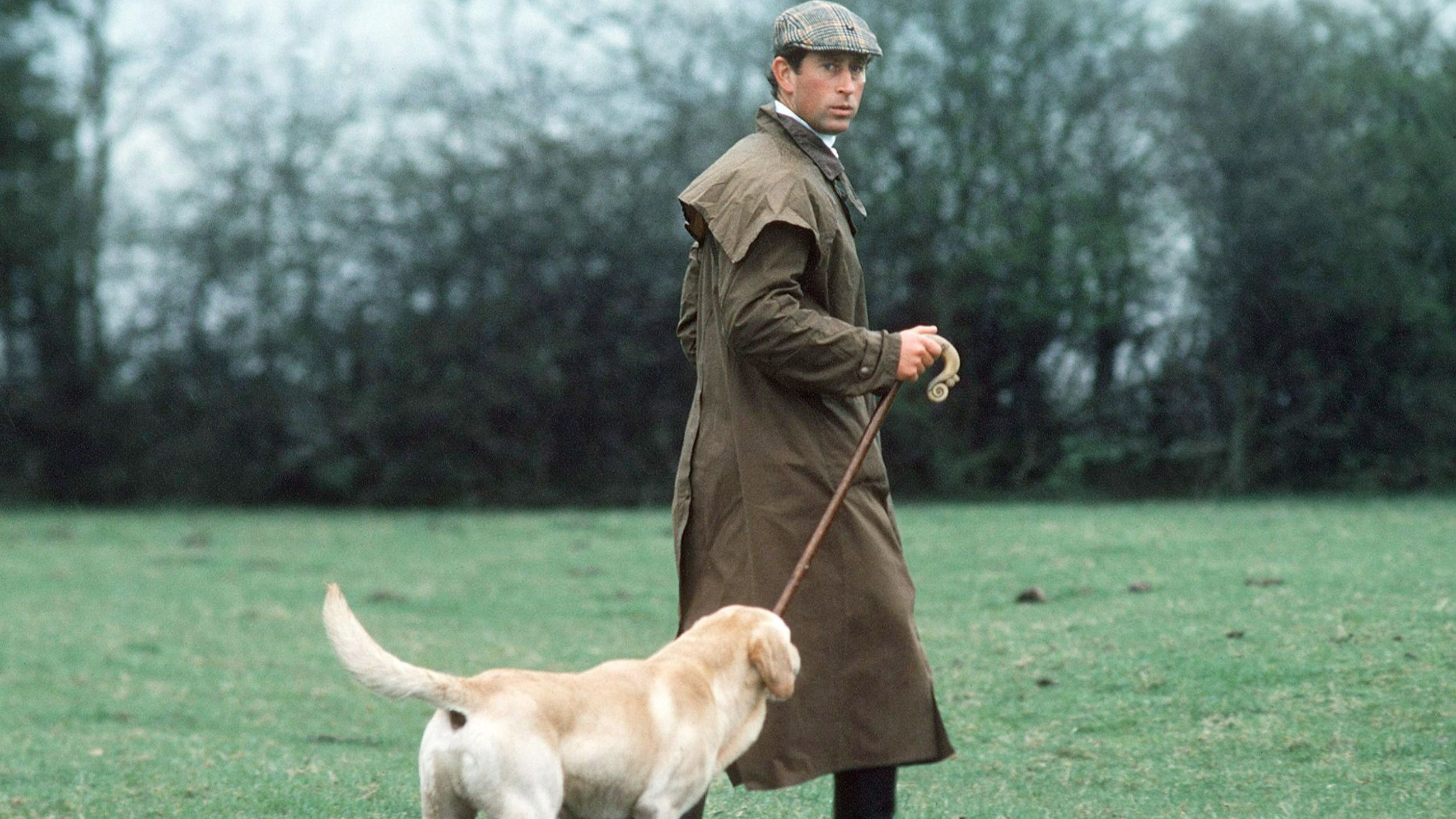 Il Principe Carlo all’evento della squadra di Cross Country della Fernie Hunt, sfoggiando un impermeabile in stile Barbour/Driza-Bone, un classico cappello piatto e un bastone da passeggio, accompagnato dal suo fedele Labrador, Harvey - Credits: Getty Images