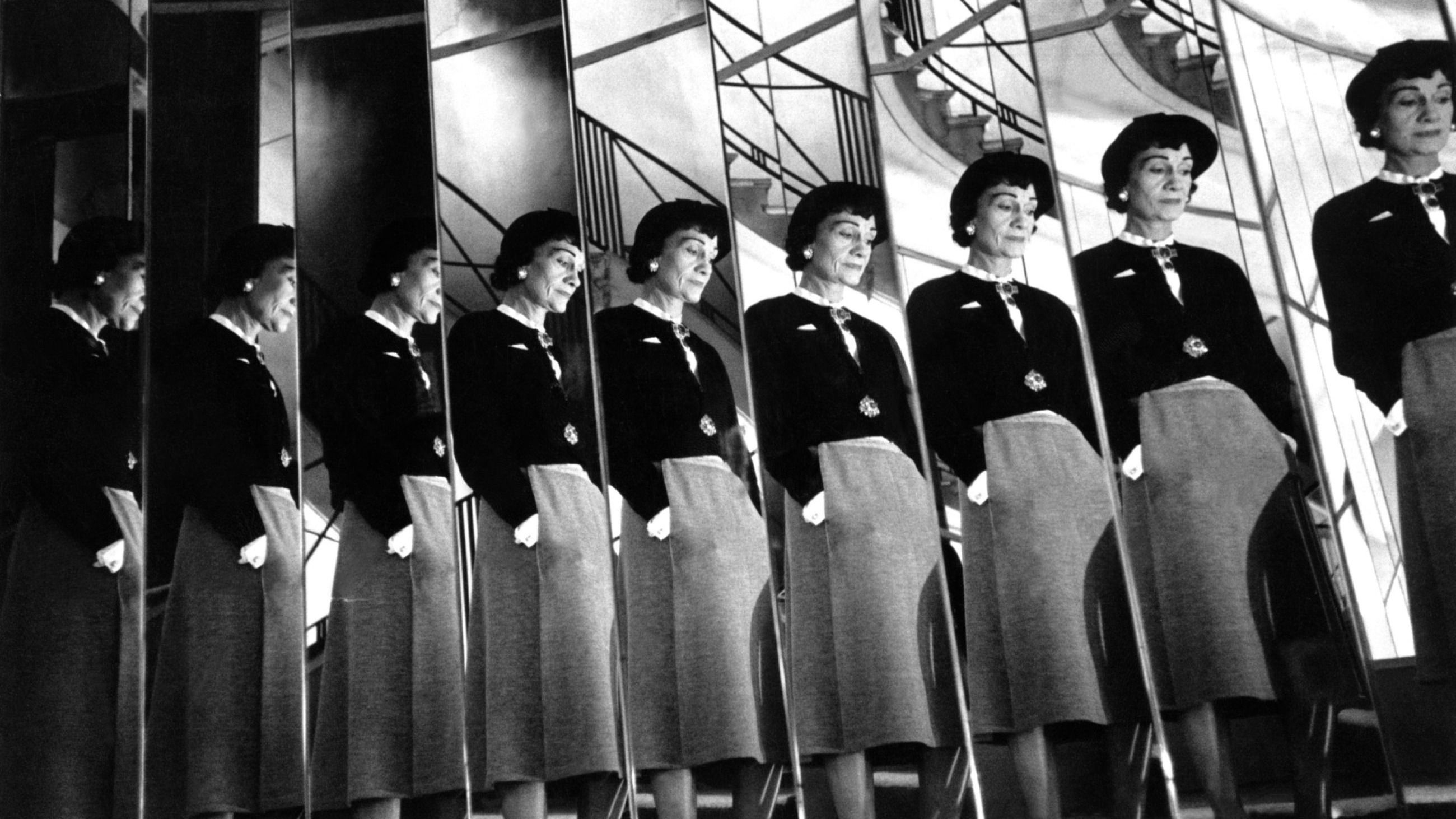 Gabrielle Chanel riflessa negli specchi che affiancano la famosa scalinata del suo appartamento in Rue Camon 31, sul cui primo gradino si sedeva per osservare le reazioni del pubblico alle sue sfilate, Parigi, 1954 - Credits: Ufficio stampa