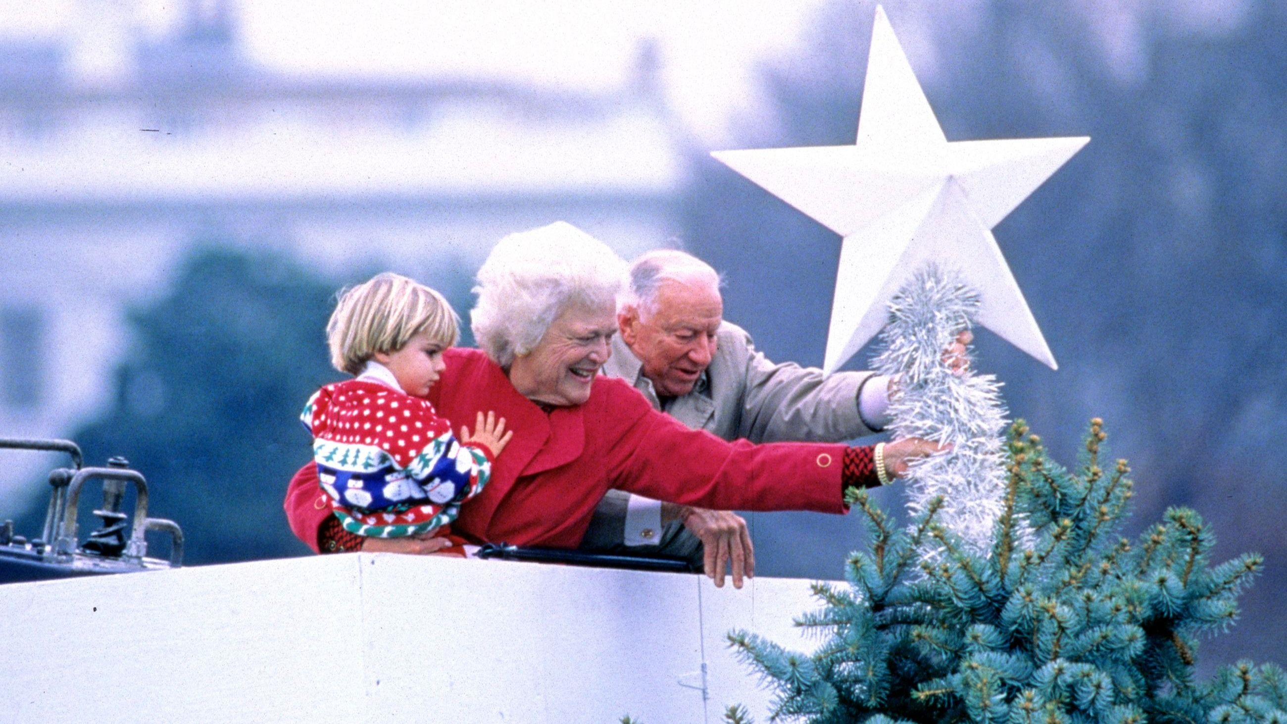 Barbara Bush tiene in braccio suo nipote, Walker Bush, mentre lei e Joseph H Riley posizionano una stella ornamentale sulla cima dell'Albero di Natale Nazionale nell'Ellisse, a Washington DC - Credits Getty Images 