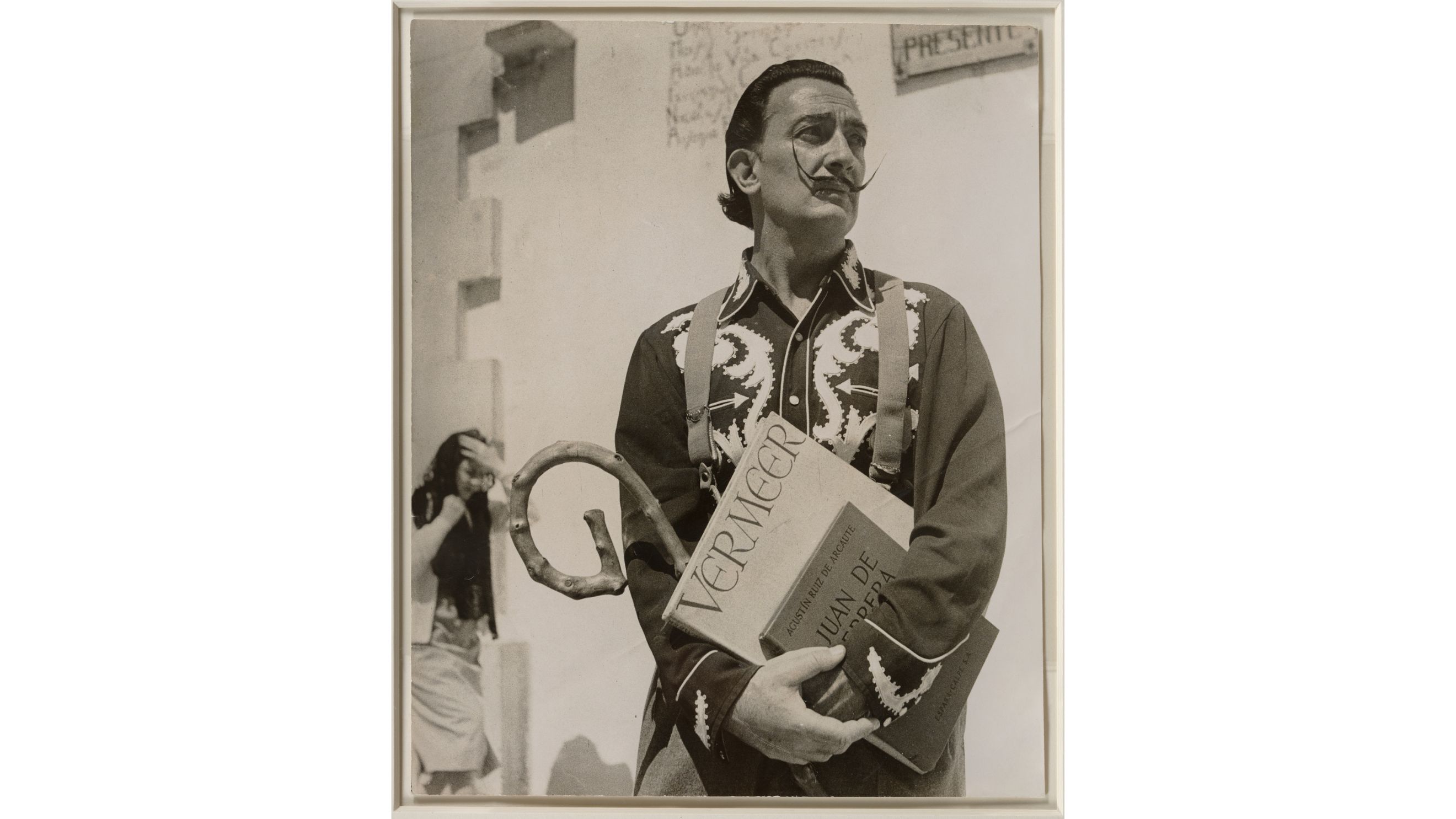 Francesc Català Roca, Salvador Dalí con i libri “The Paintings of Jan Vermeer” e “Juan de Herrera arquitecto de Filippo II” davanti alla chiesa di Cadaqués / Salvador Dalí con los libros "The Paintings of Jan Vermeer" y "Juan de Herrera arquitecto de Felipe II" delante de la iglesia de Cadaqués 1957, Riproduzione fotografica © FRANCESC CATALA ROCA, by SIAE 2025. Derechos de imagen de Salvador Dalí reservados. Fundació Gala-Salvador Dalí, Figueres, 2025 - Courtesy Press Office