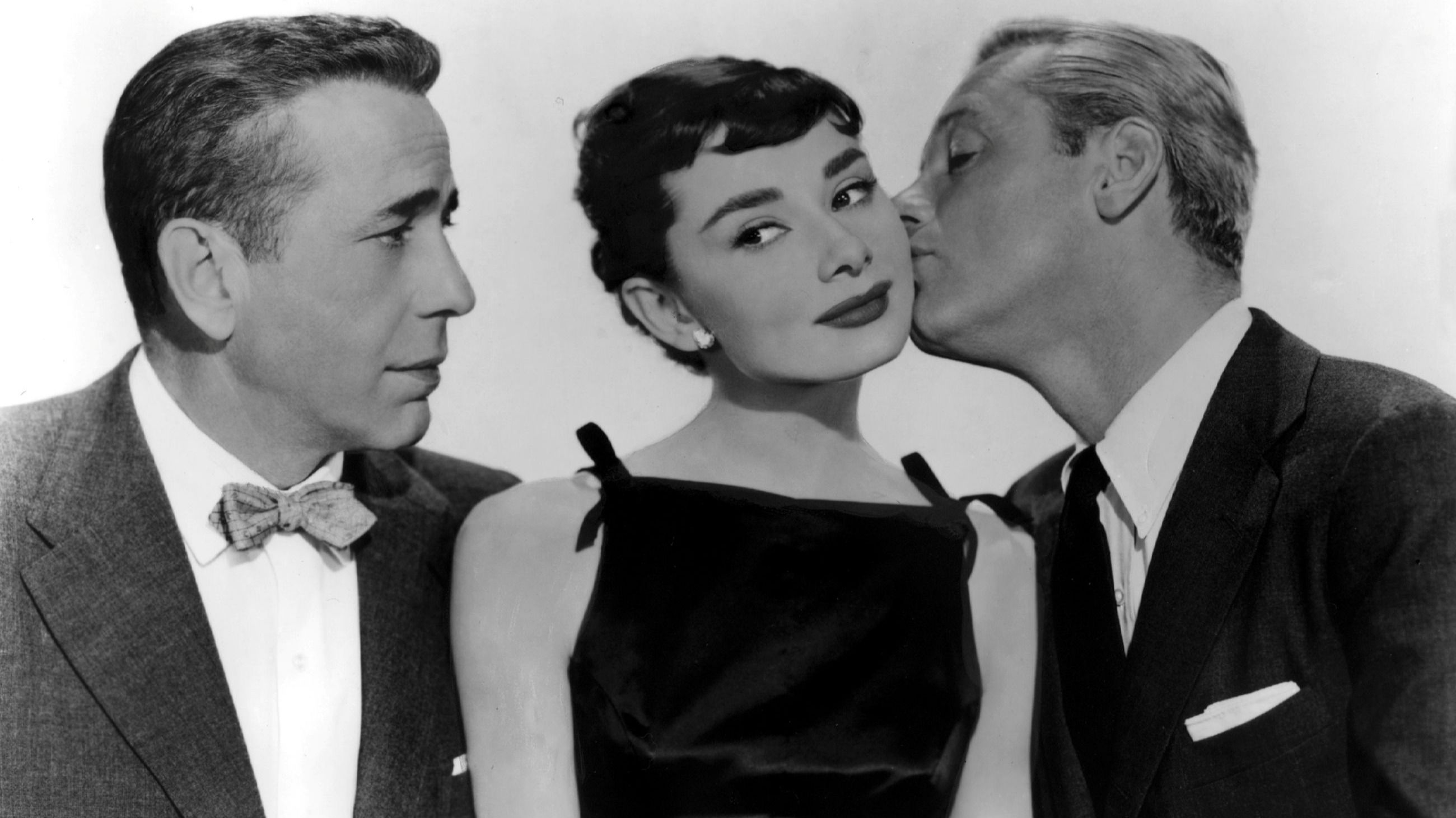 Audrey Hepburn posa, insieme agli attori e colleghi Humphrey Bogart e William Holden, per il film “Sabrina” del 1954. L’attrice, qui, sfoggia un little black dress dalla scollatura a barchetta, divenuta iconica anche grazie a lei e al suo stile intramontabile - Credits: Getty Images
