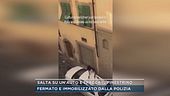 Salta su un'auto e spacca il finestrino